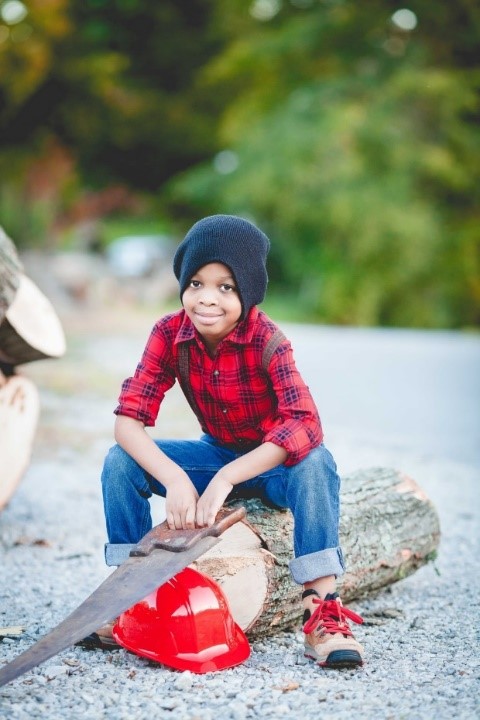 Smiling soy sitting on top of cut tree log with saw in hand