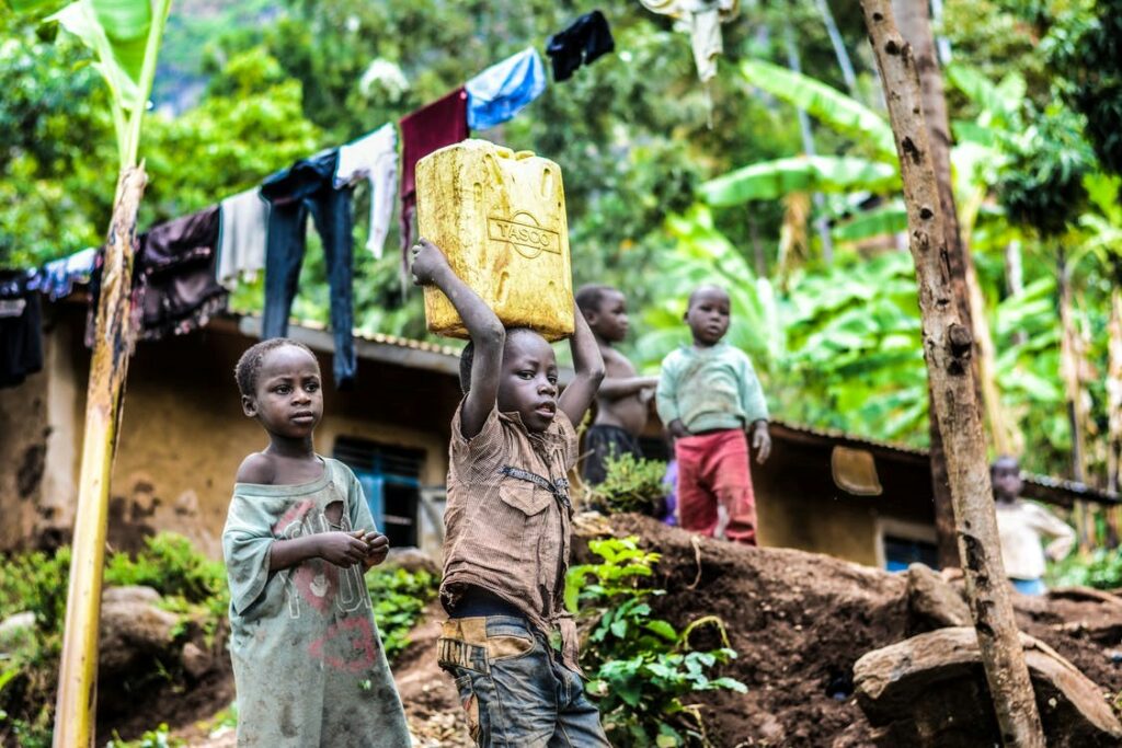 Young boys in worn clothing, one carrying a load on his head