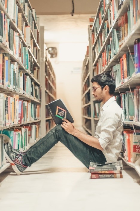 Young man reading while sitting on floor between library shelves